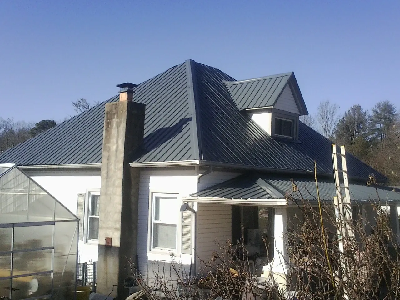 Dark blue standing seam metal roof on a white farmhouse with dormer — Slate & Tile Roof Repair by Roofing Brothers in Rudolph
