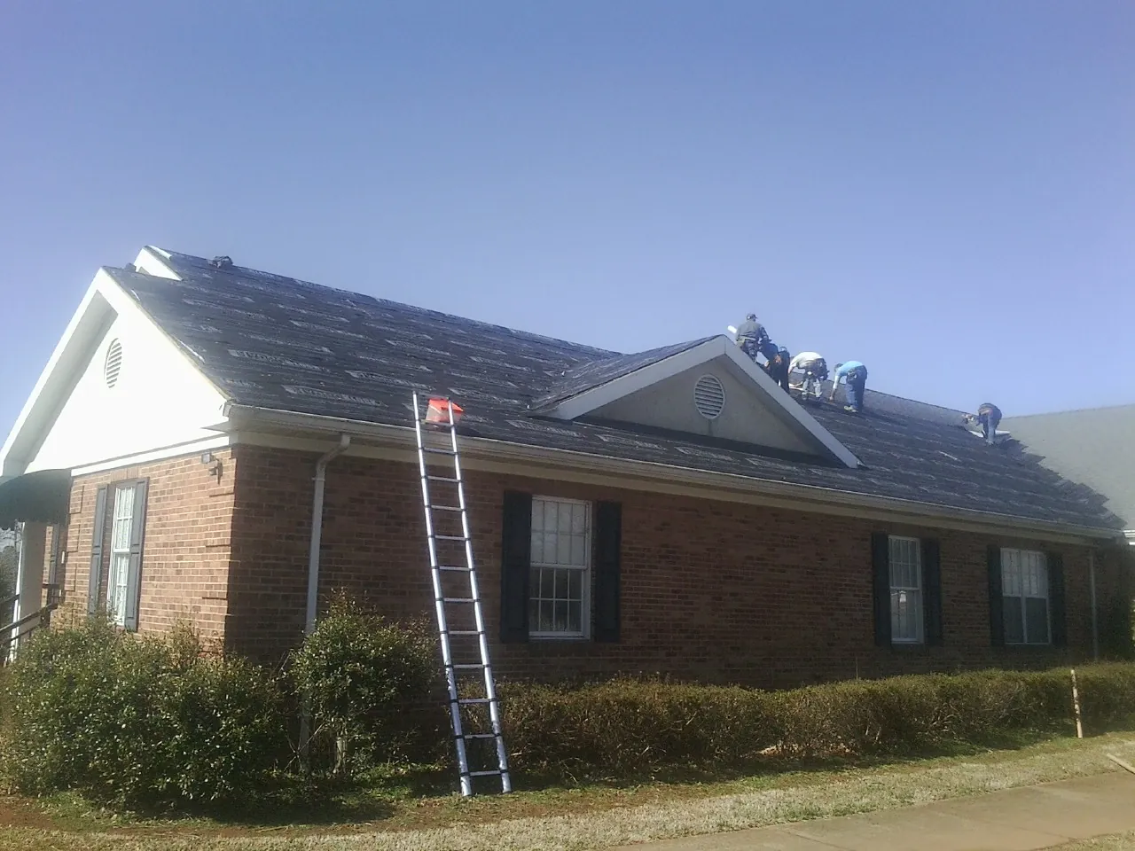 Crew tearing shingles off a brick ranch roof with a ladder set — Metal Roof Repair work by our crew in Rudolph