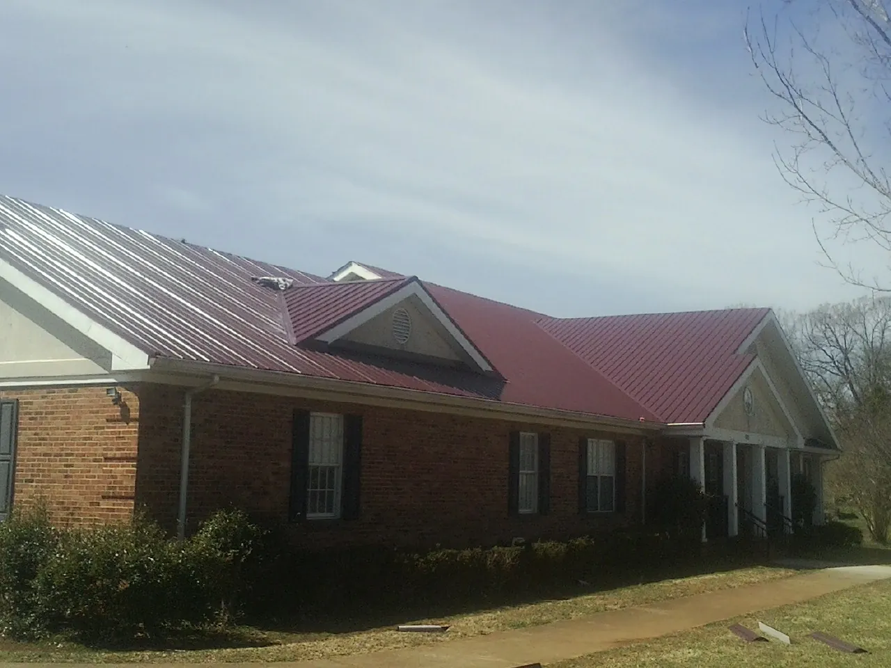 Red metal roof with gabled entries on a long brick building, from a Hail Damage Roof Repair job in Rudolph