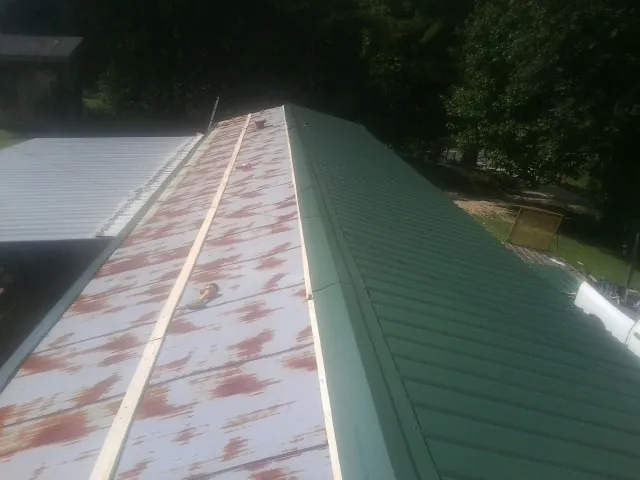 Old rusted panels beside newly installed green metal roofing — Wind Damage Roof Repair by Roofing Brothers in Rudolph