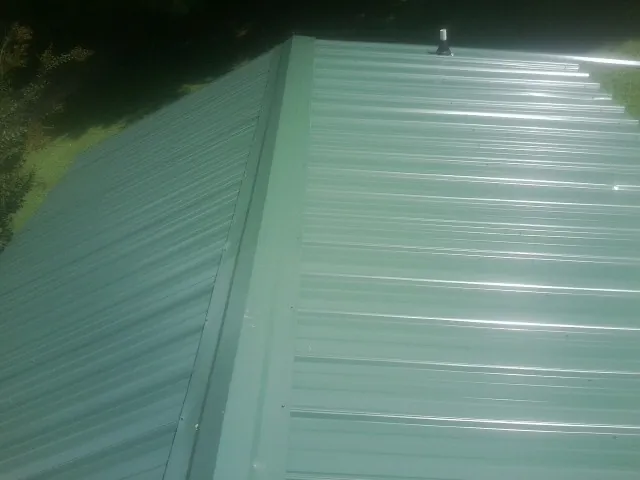 New green metal panels meeting at the ridge of a roof — Flat Roof Repair work by our crew in Rudolph