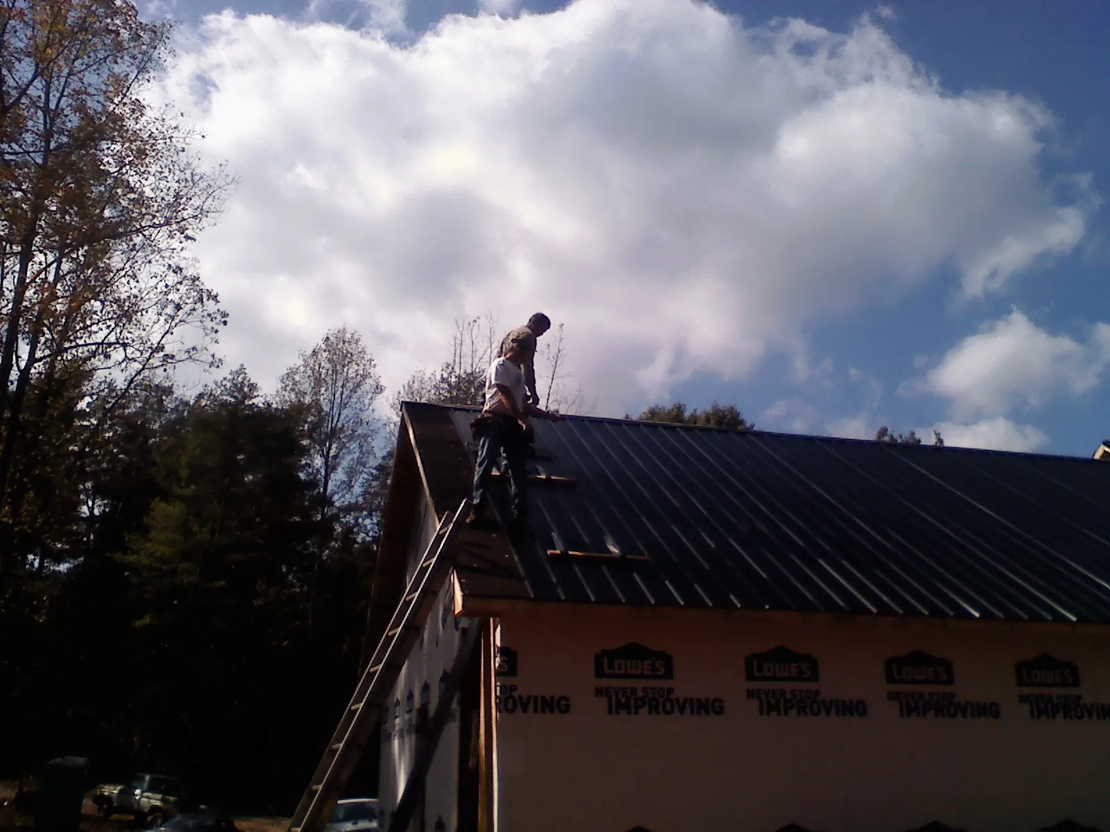 Roofer fastening dark metal panels high against a cloudy sky, from a Roof Inspection job in Rudolph