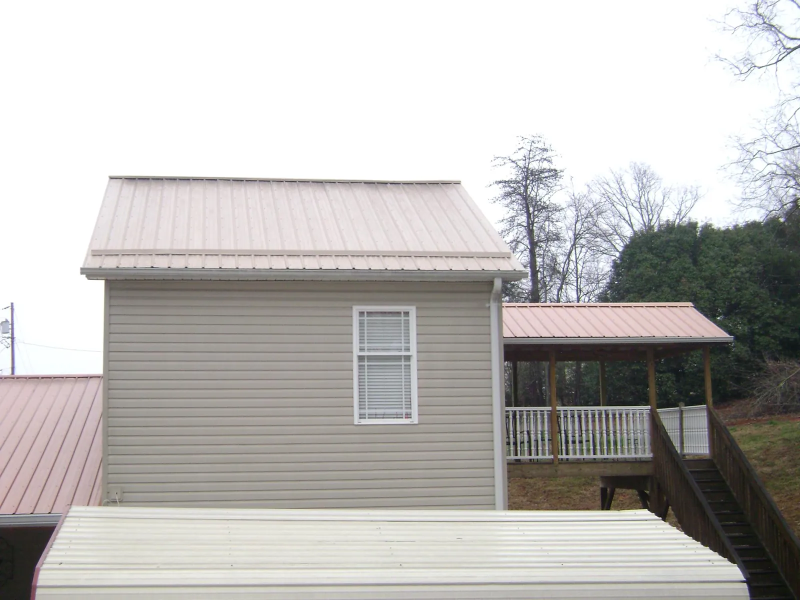 Tan metal roofs on a two story addition and attached porch, from a Roof Replacement job in Rudolph