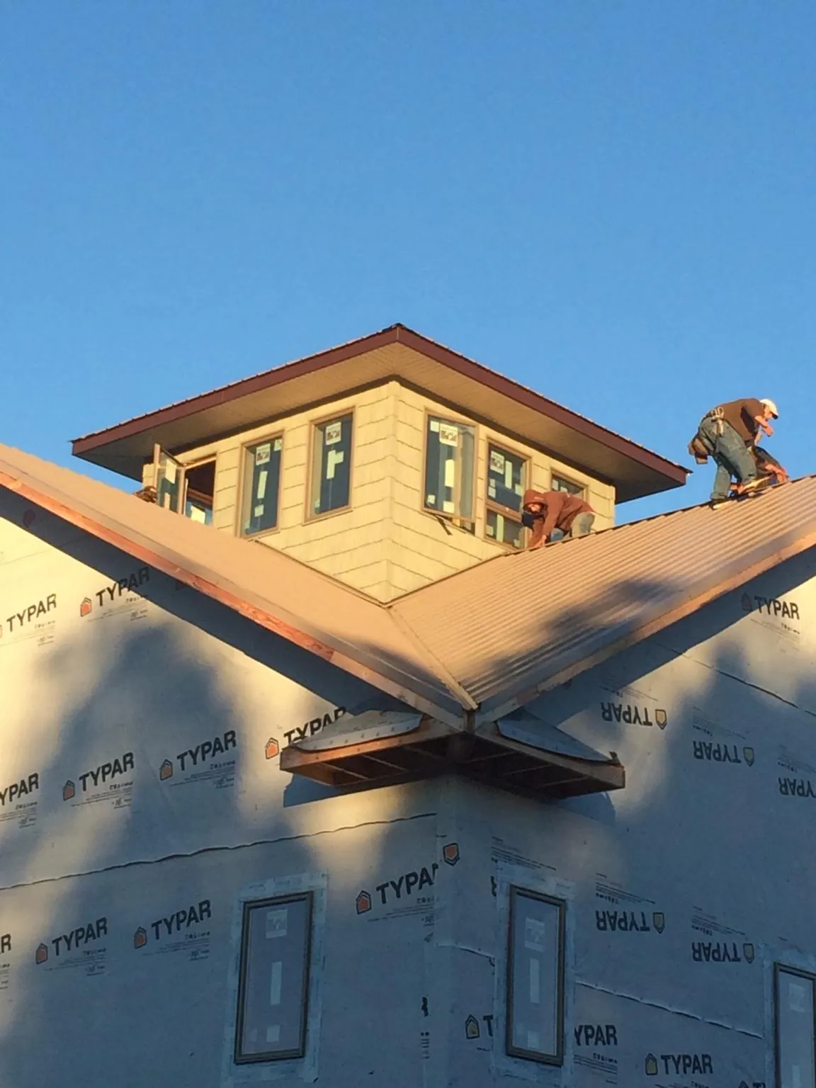 Roofers working around a rooftop cupola on a new metal roof at sunset — Roof Waterproofing in Rudolph by Roofing Brothers
